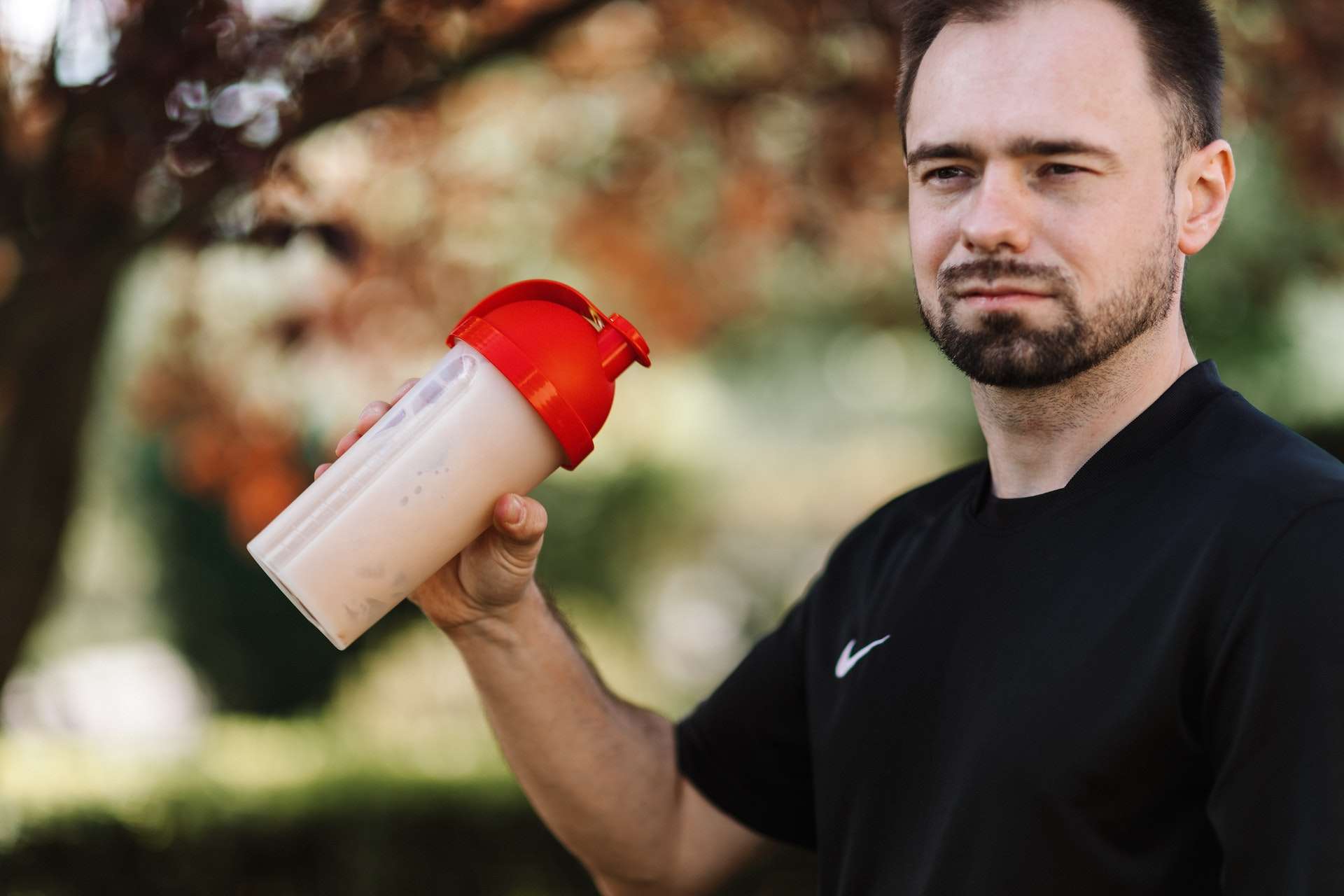 A Bearded Man Holding a Plastic Tumbler With Red Lid 