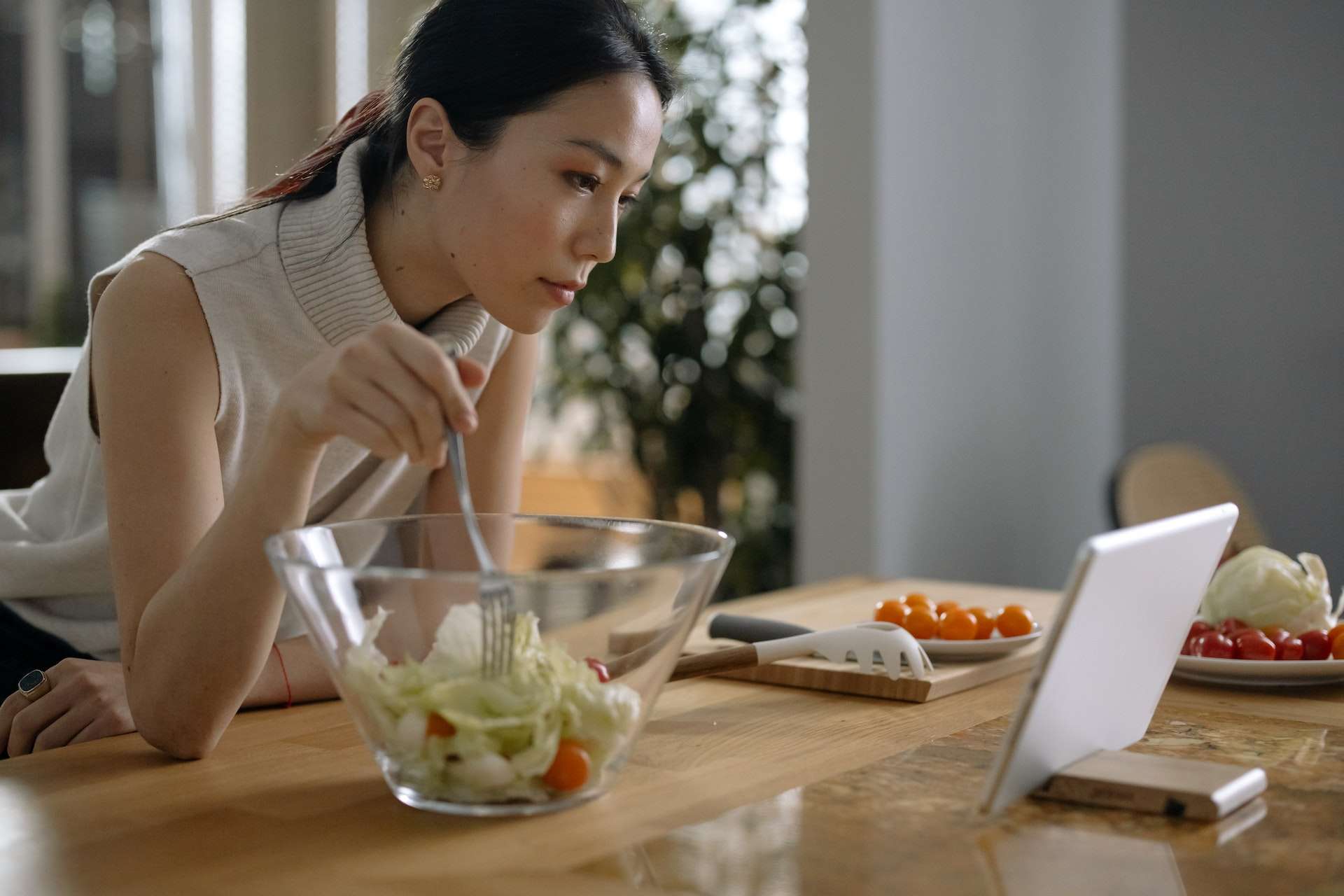 A Woman Looking at the Digital Tablet while eating his vegetable salad