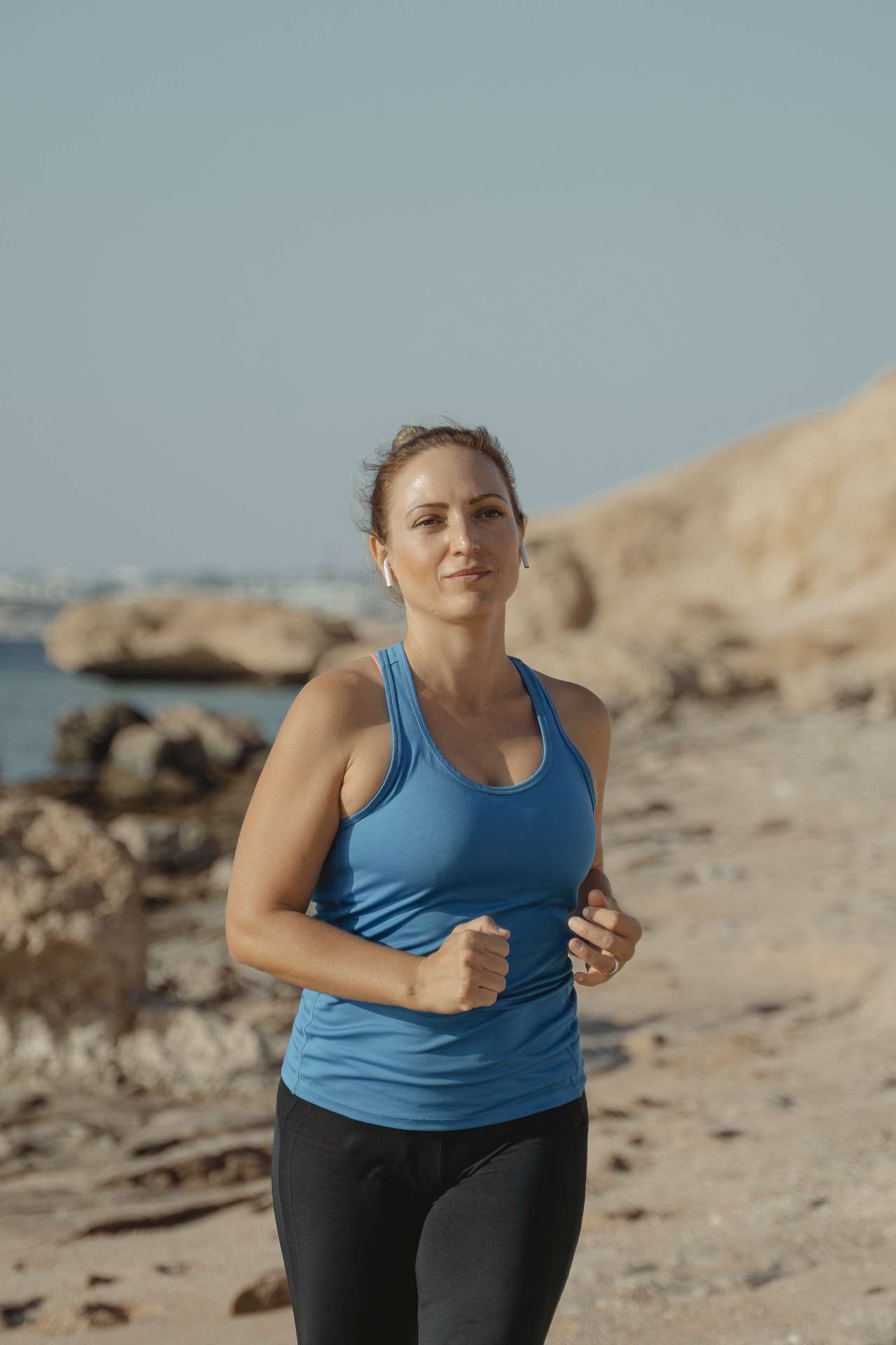 A Woman in Blue Tank Top Running on the Beach 
