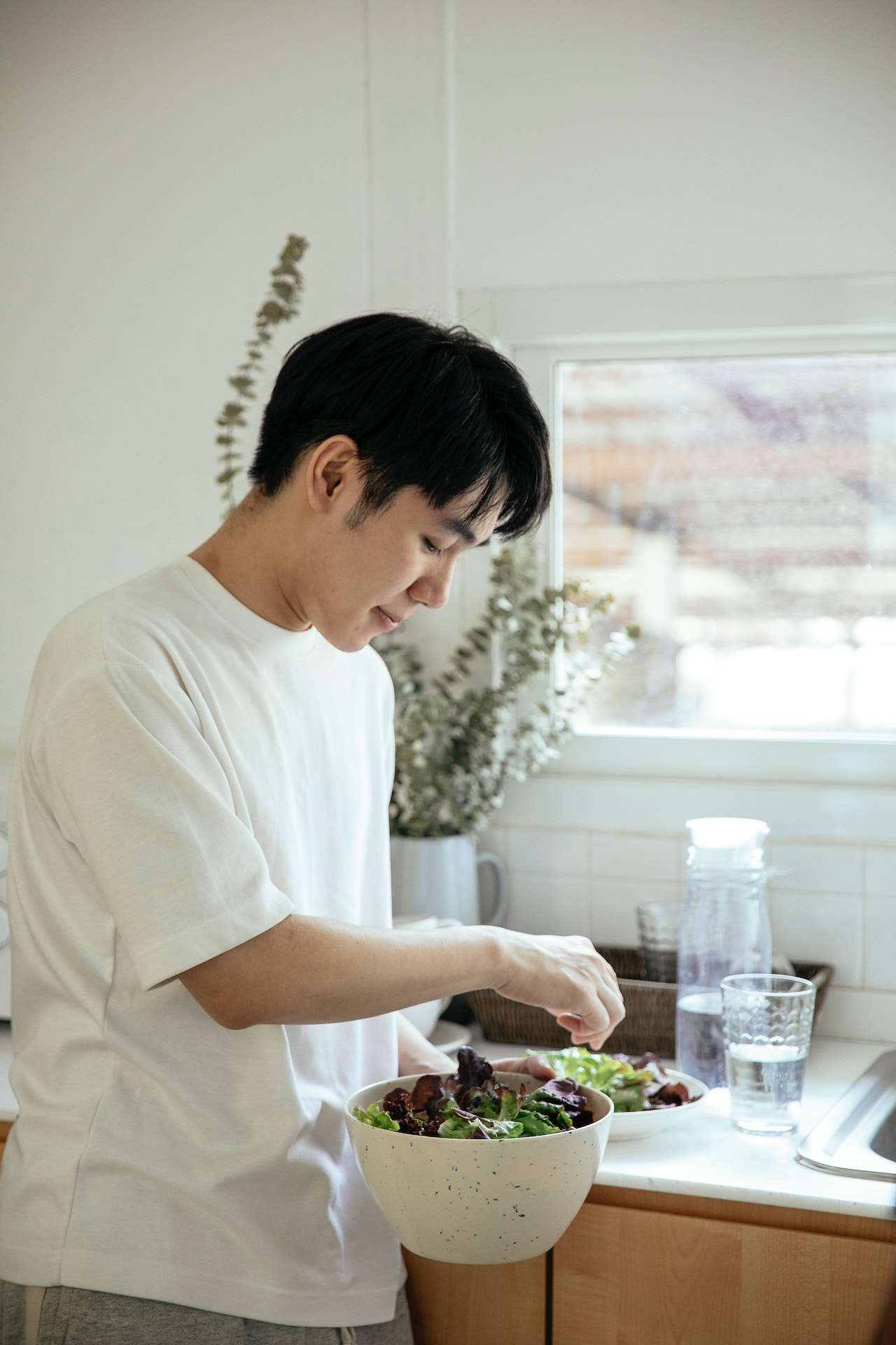 Asian man serving salad into plate 