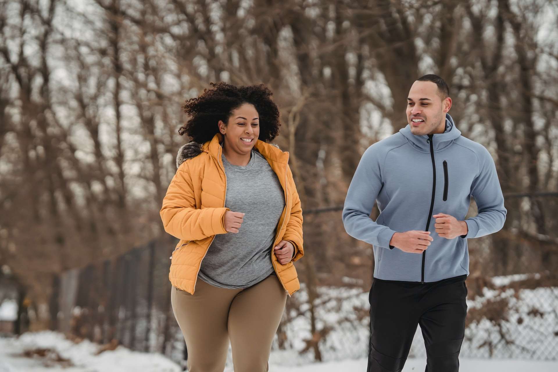 Cheerful multiethnic man and woman running together in winter park 