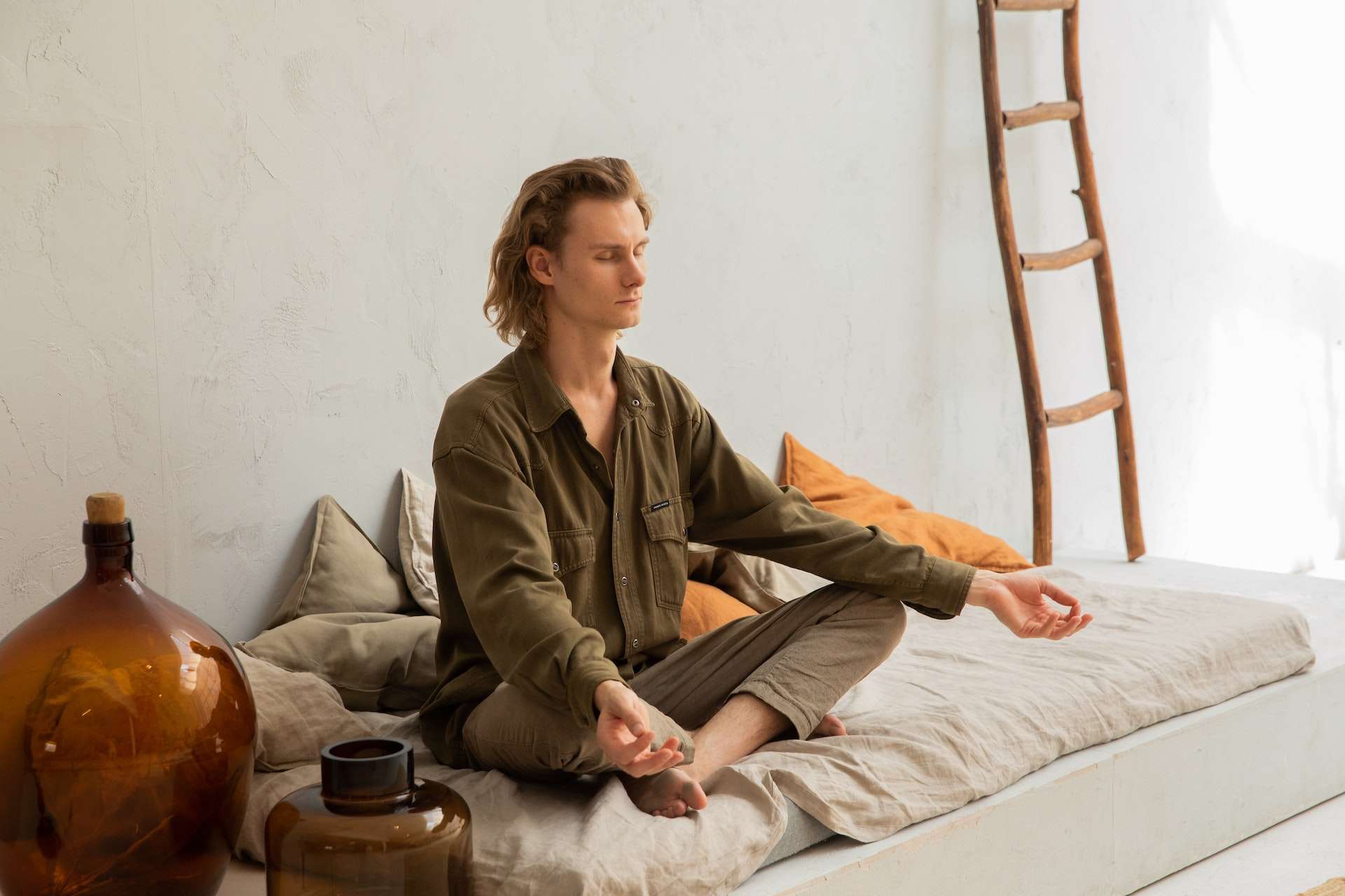 Concentrated man meditating in Lotus pose on mattress