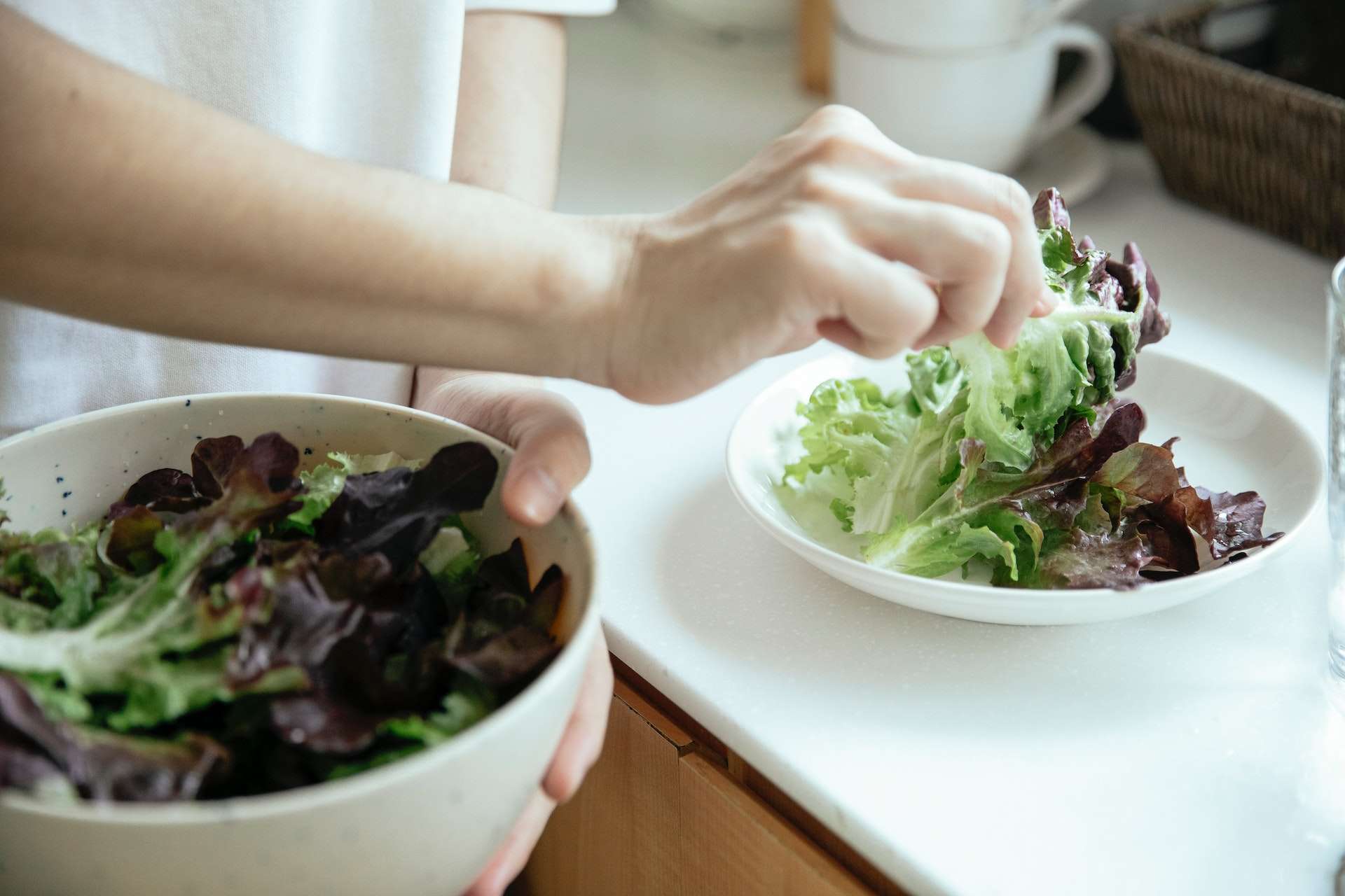 Crop person putting salad into plate from bowl