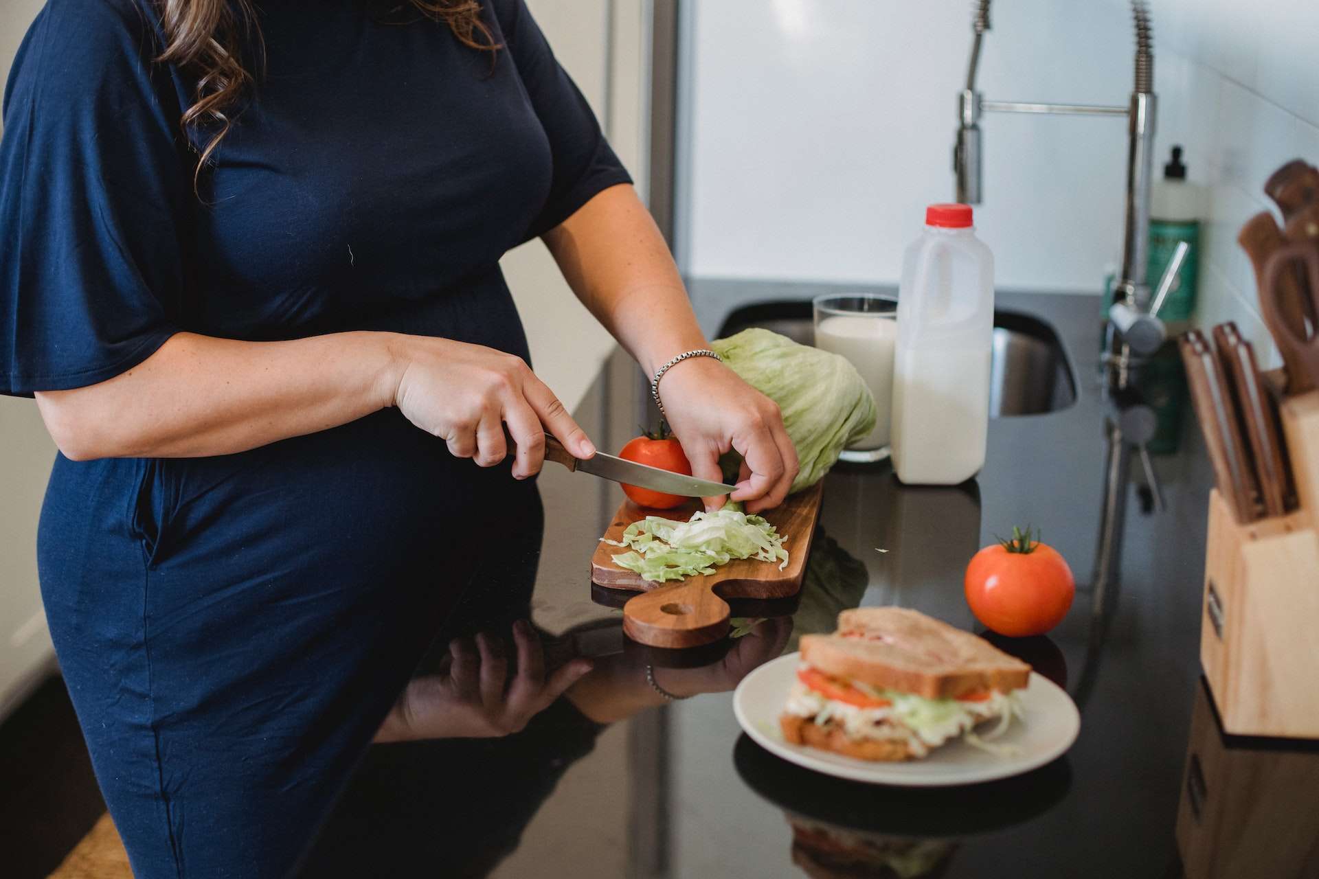 Crop pregnant woman chopping lettuce leaves in modern kitchen 