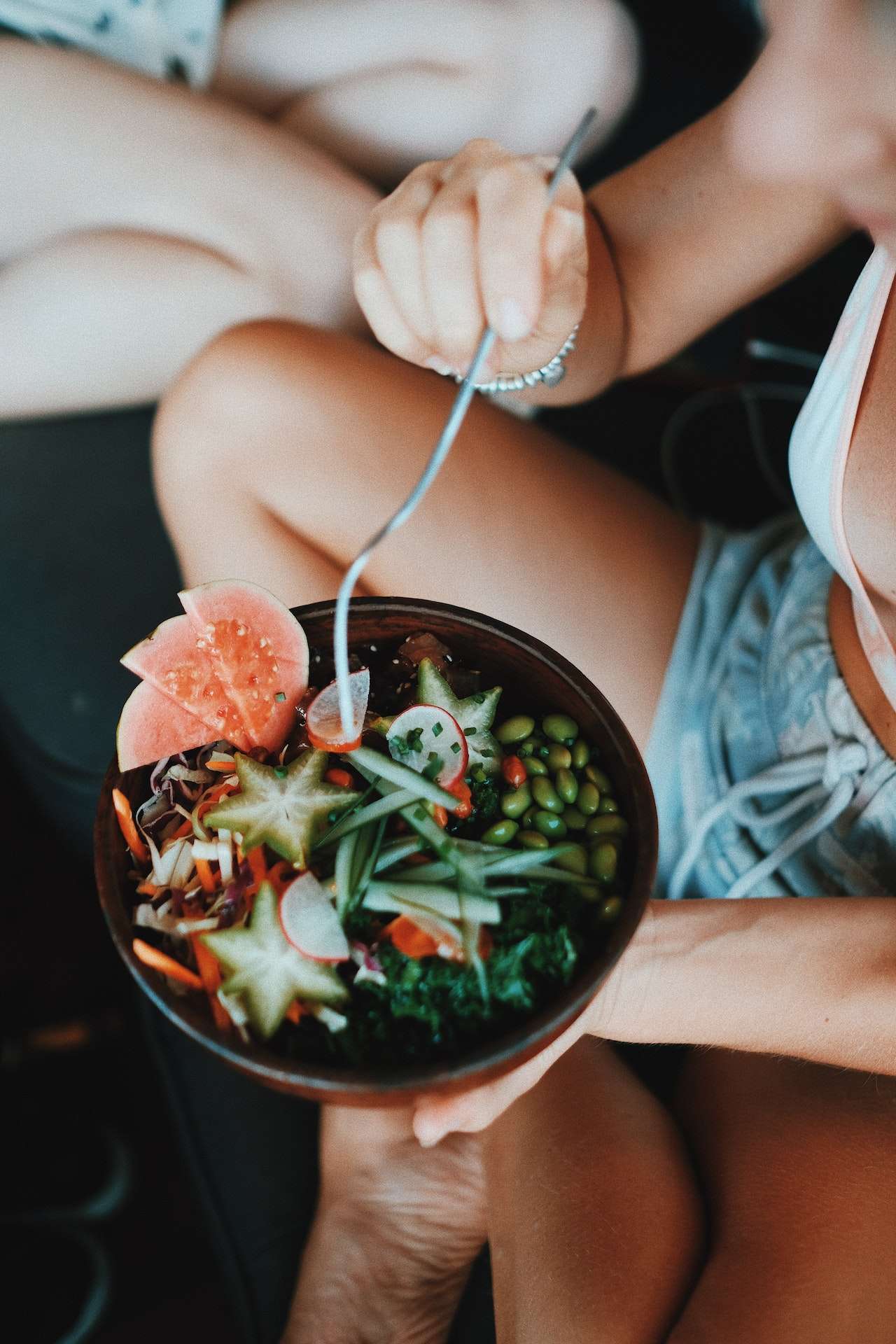 Crop young female tourist eating fresh vegan salad in resort cafe 