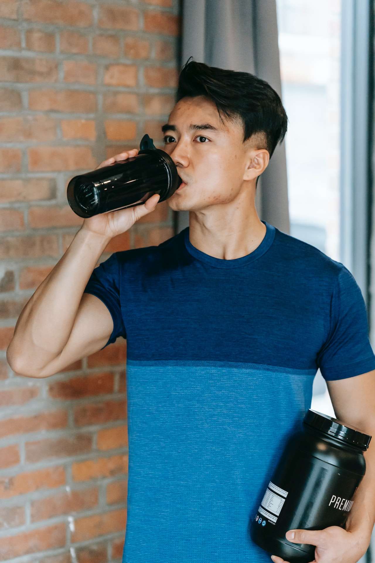 Determined young ethnic guy drinking water during training in gym 