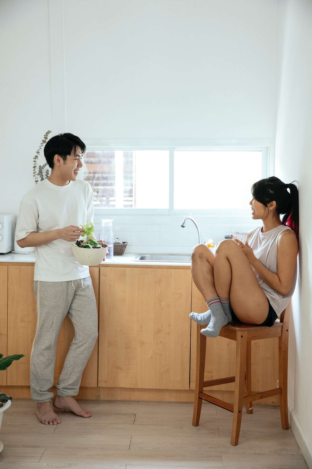 Ethnic couple in kitchen near counter eating vegetarian salad