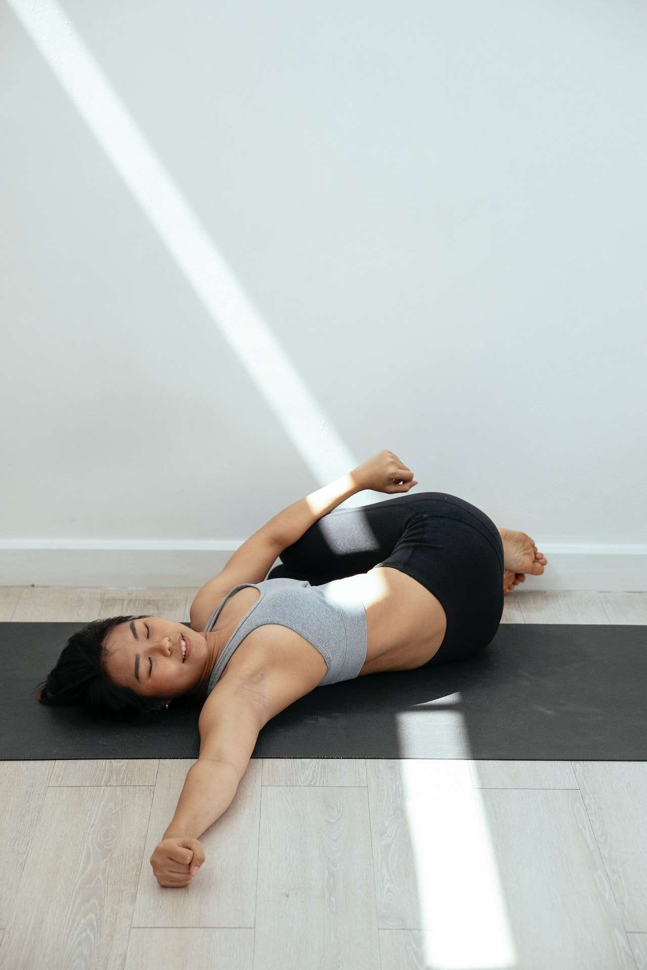 Fit Asian woman doing Supine Spinal Twist on yoga mat 