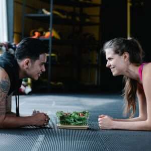 Man and Woman at the Gym Doing Planks while Looking at Each Other and Smiling