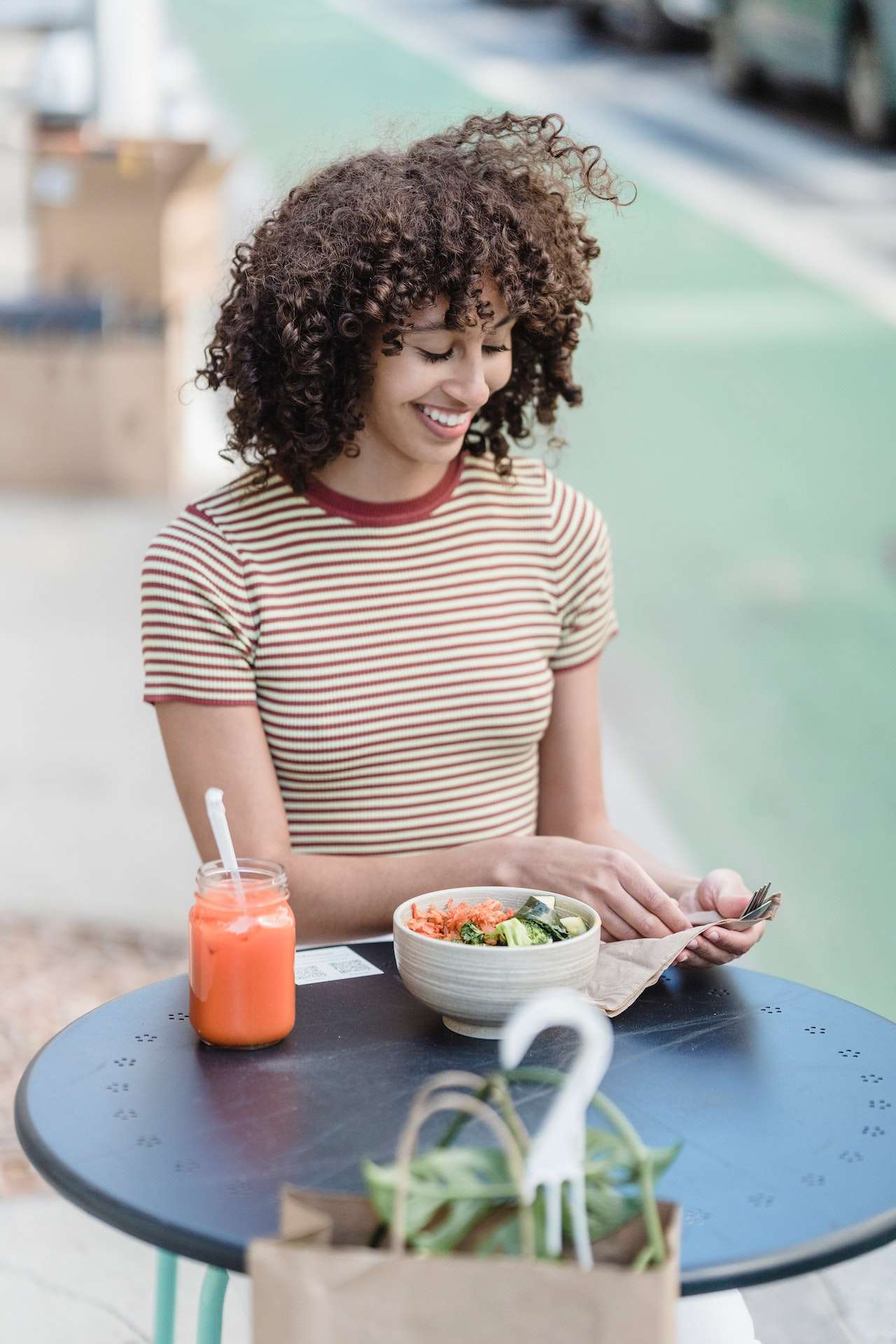 Smiling ethnic woman with vegetable salad and smoothie in cafe