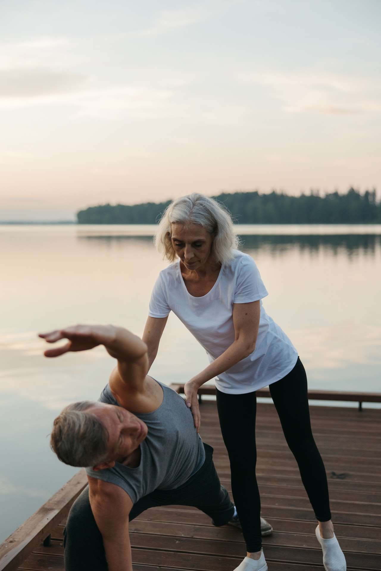 Woman in White Crew Neck T-shirt Holding the Man while He's Exercising 
