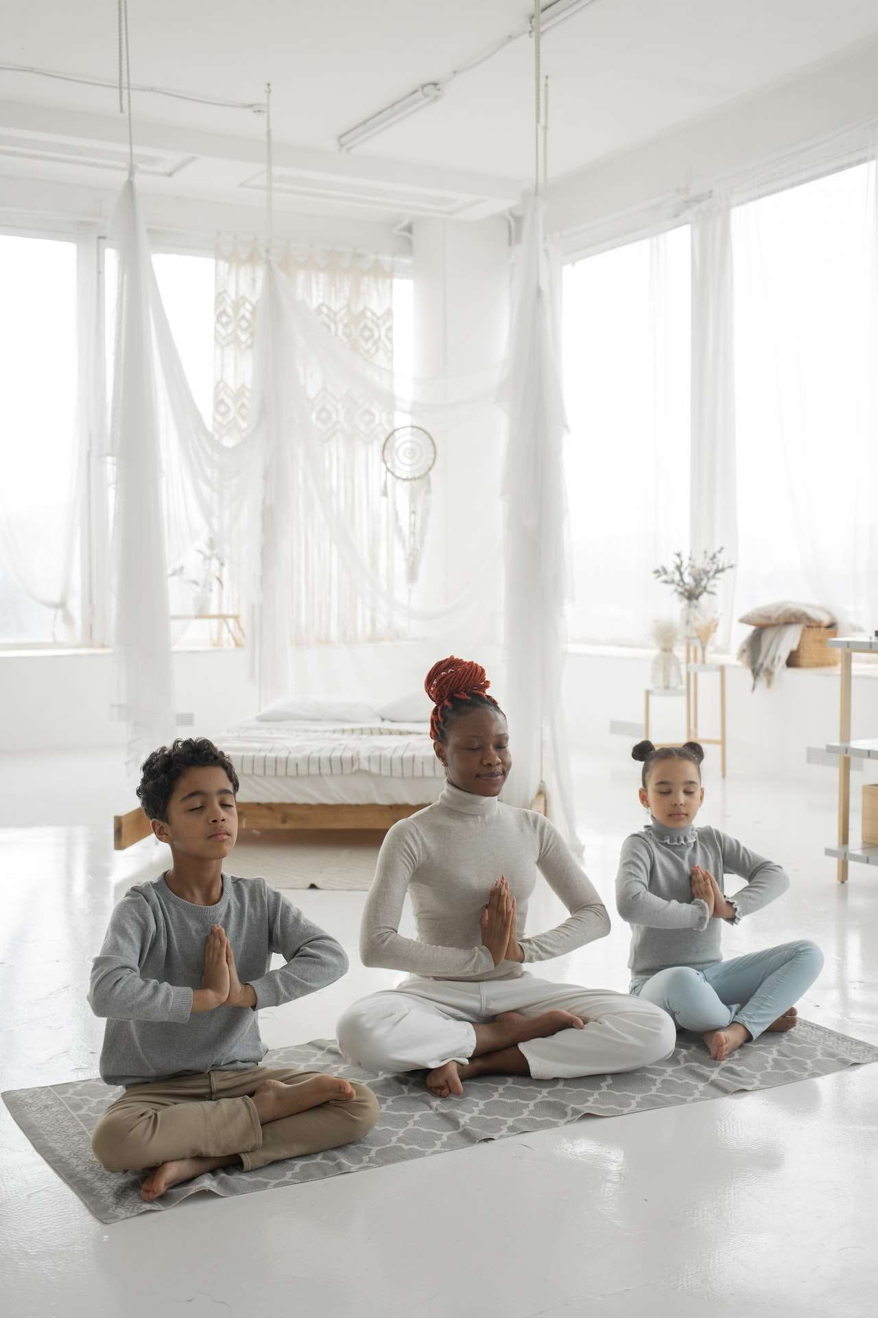 Young ethnic mother with cute children practicing yoga together at home 