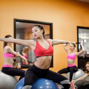 Young flexible multiracial women practicing pilates on fit ball in modern studio