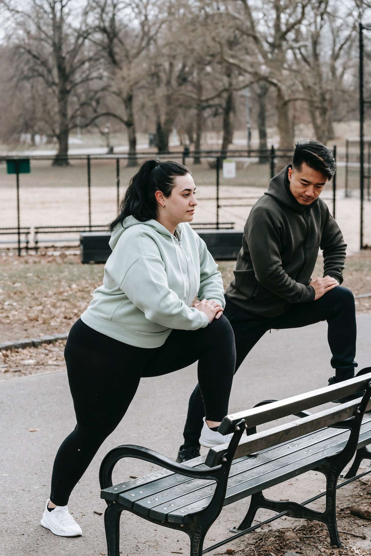 Young obese female with ethnic male instructor exercising together in park 