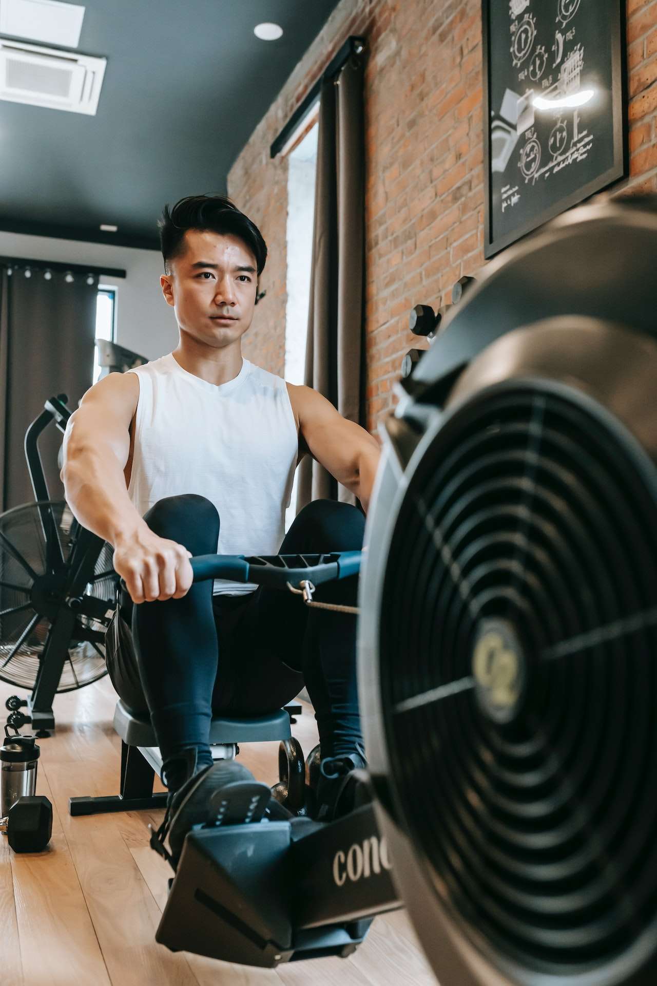 Concentrated Asian sportsman exercising on rowing machine 