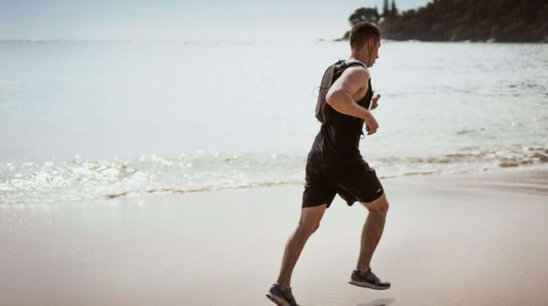 Man Wearing Black Tank Top and Running on Seashore