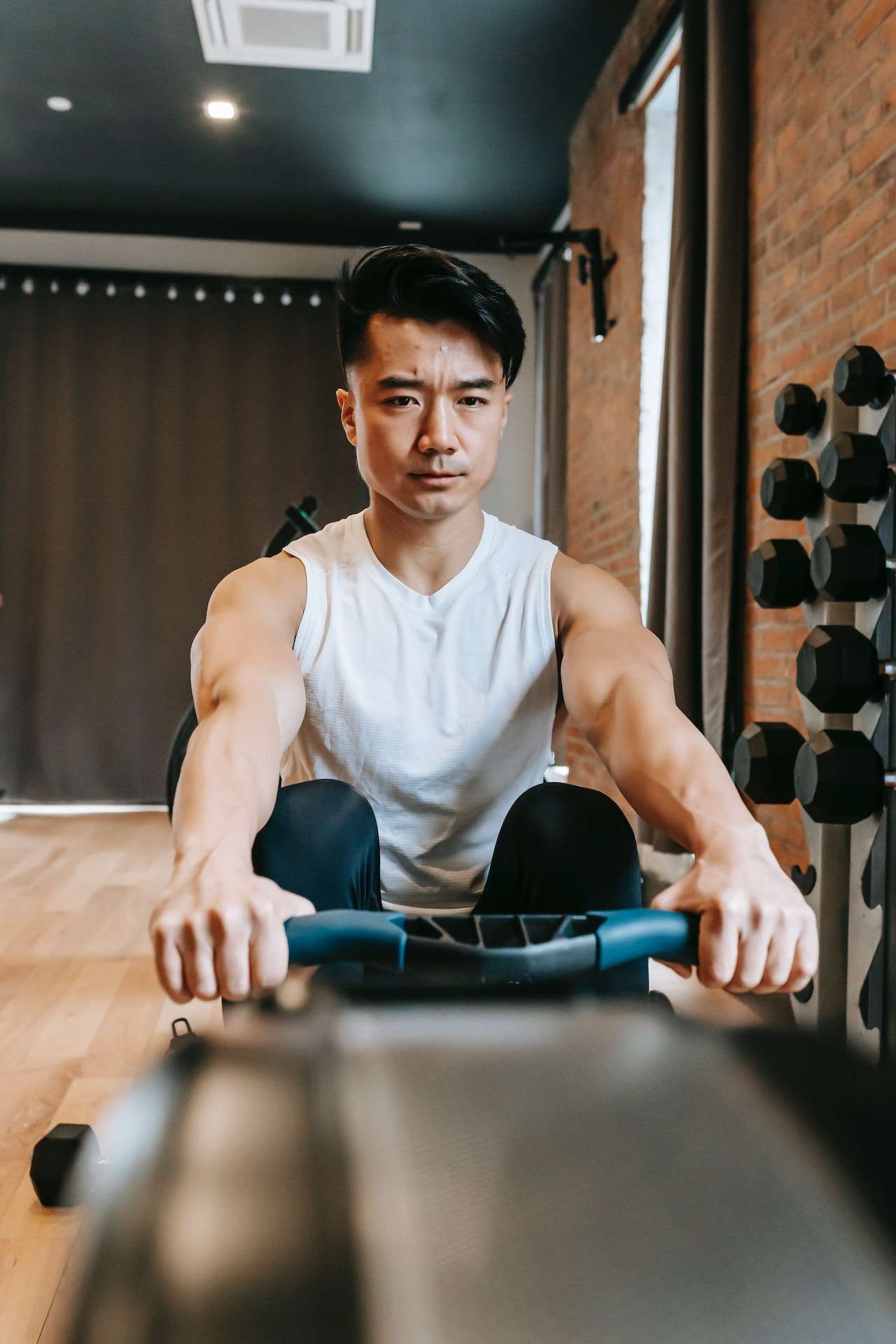 Strong Asian man training on rowing machine in gym 