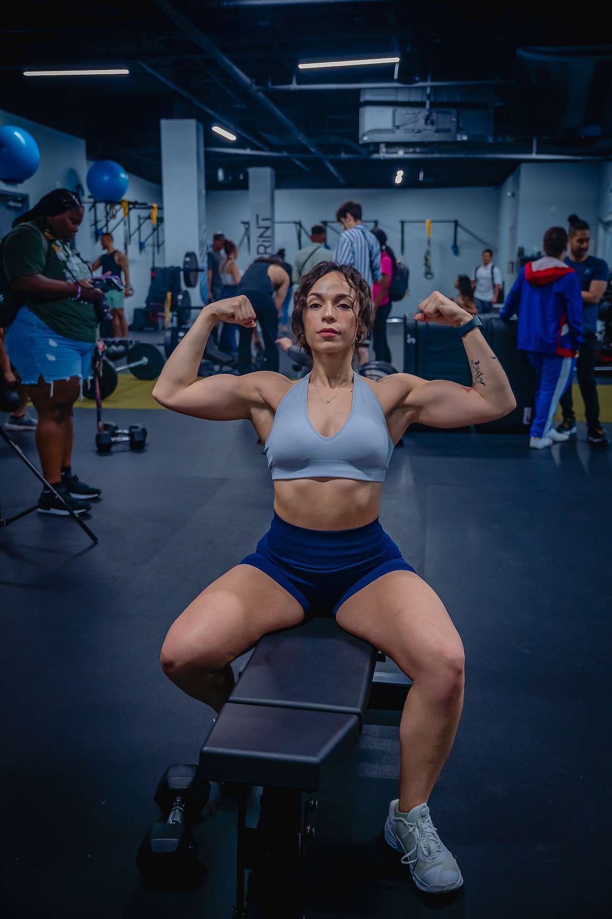 Woman Sitting in Blue Sports Bra Flexing Her Arm Muscles 