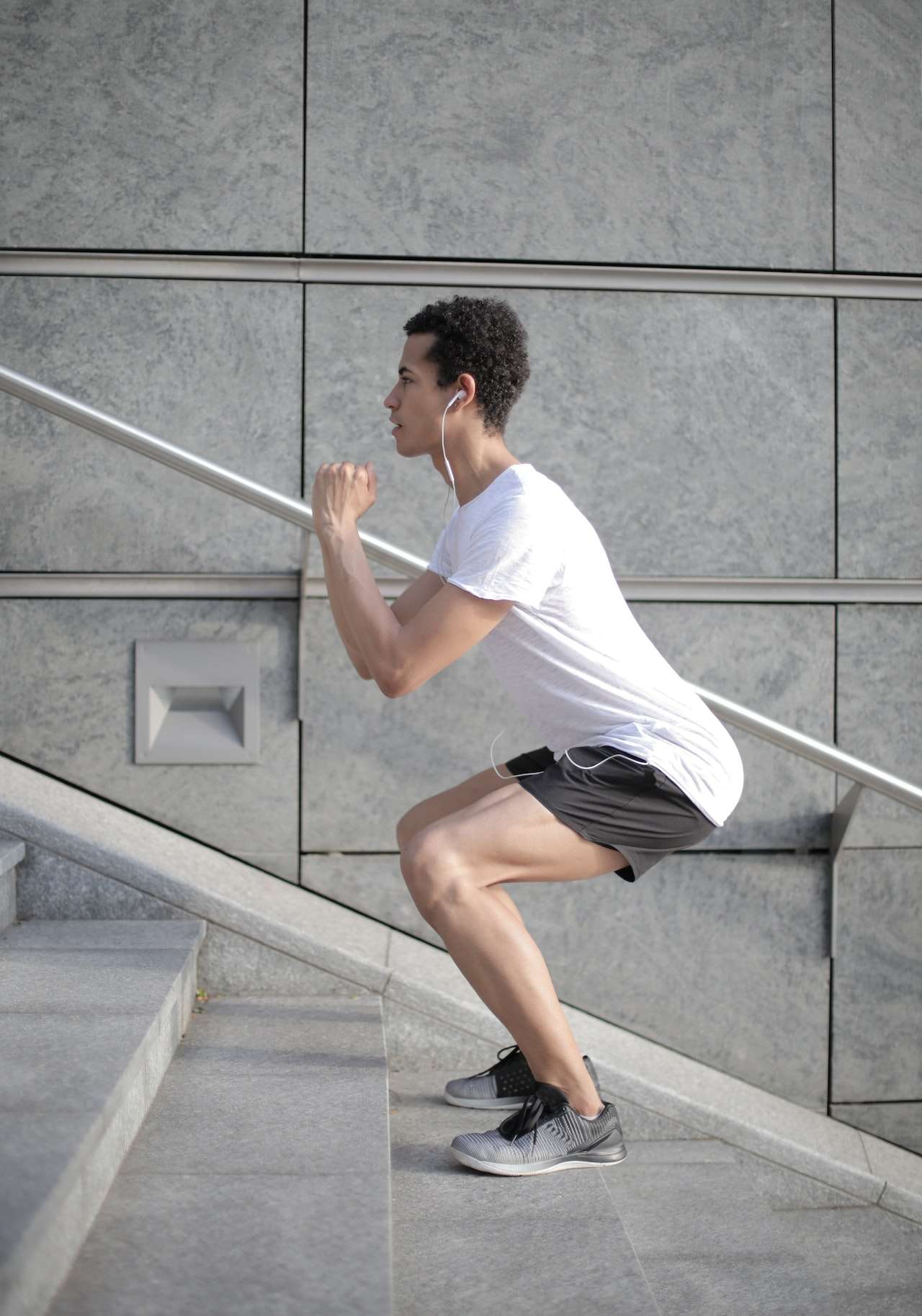 Young ethnic focused sportsman exercising on stairs in city
